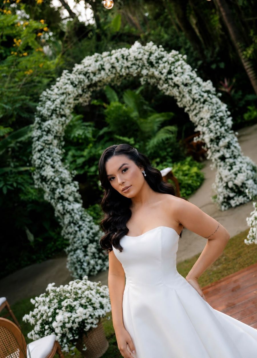 Noiva de vestido tomara que caia diante de arco de flores brancas