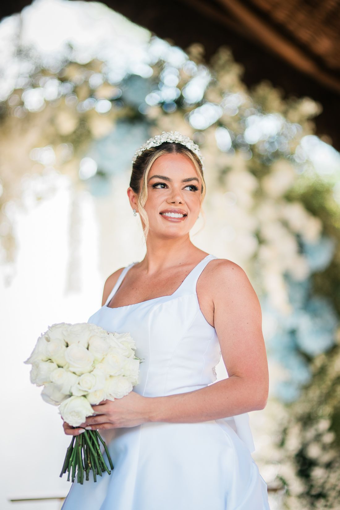 Noiva com buquê de rosas brancas sob arco de flores