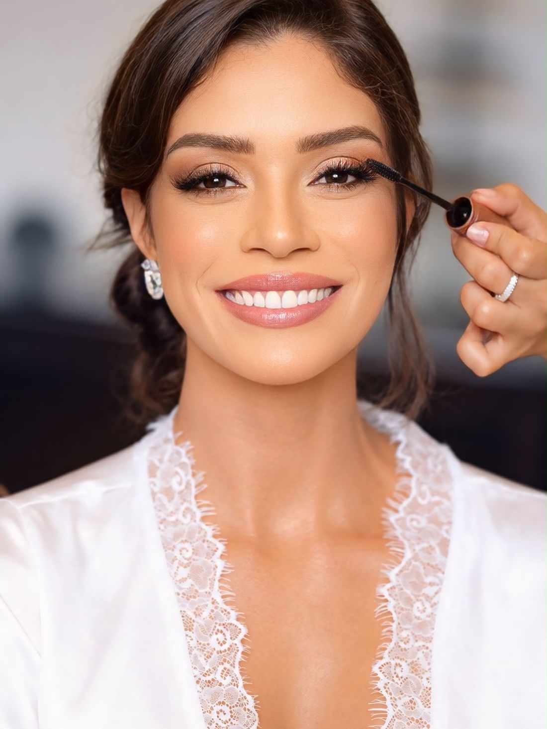 Noiva sorrindo enquanto recebe a máscara de cílios, de robe de renda