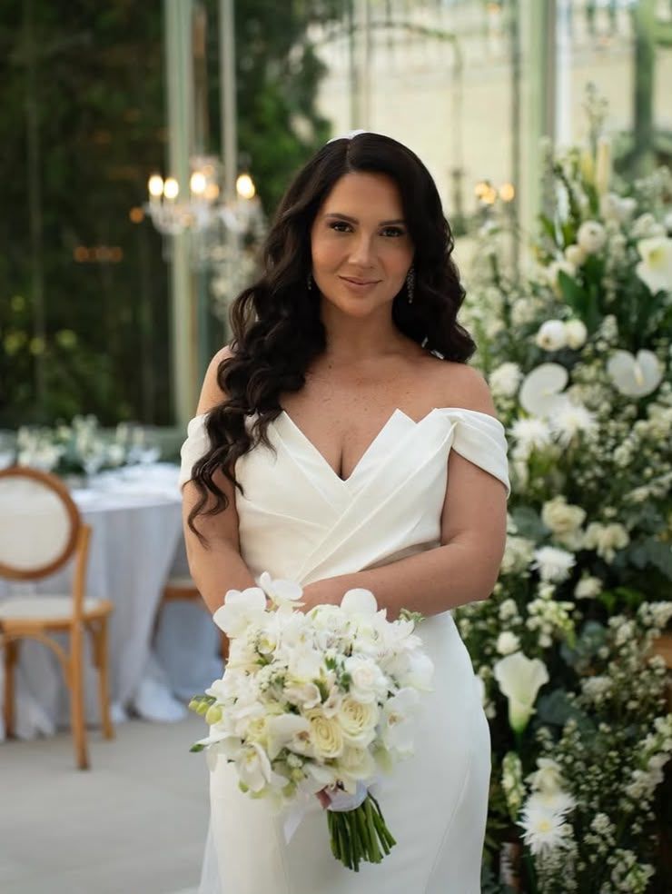 Noiva de cabelo ondulado e ombros à mostra com buquê de orquídeas