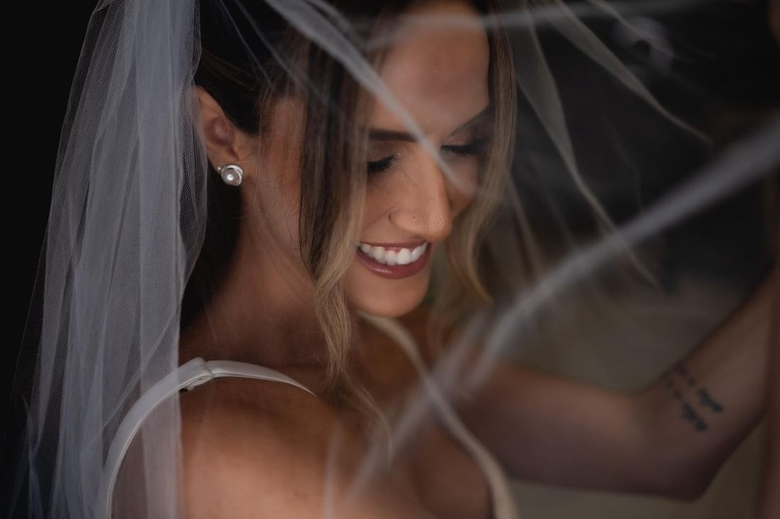 Detalhe da noiva sorrindo sob o véu, com brinco de pérola